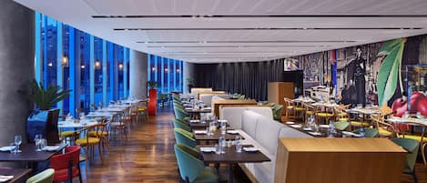 A modern restaurant with high ceilings, large windows, and a variety of seating options including booths and tables.