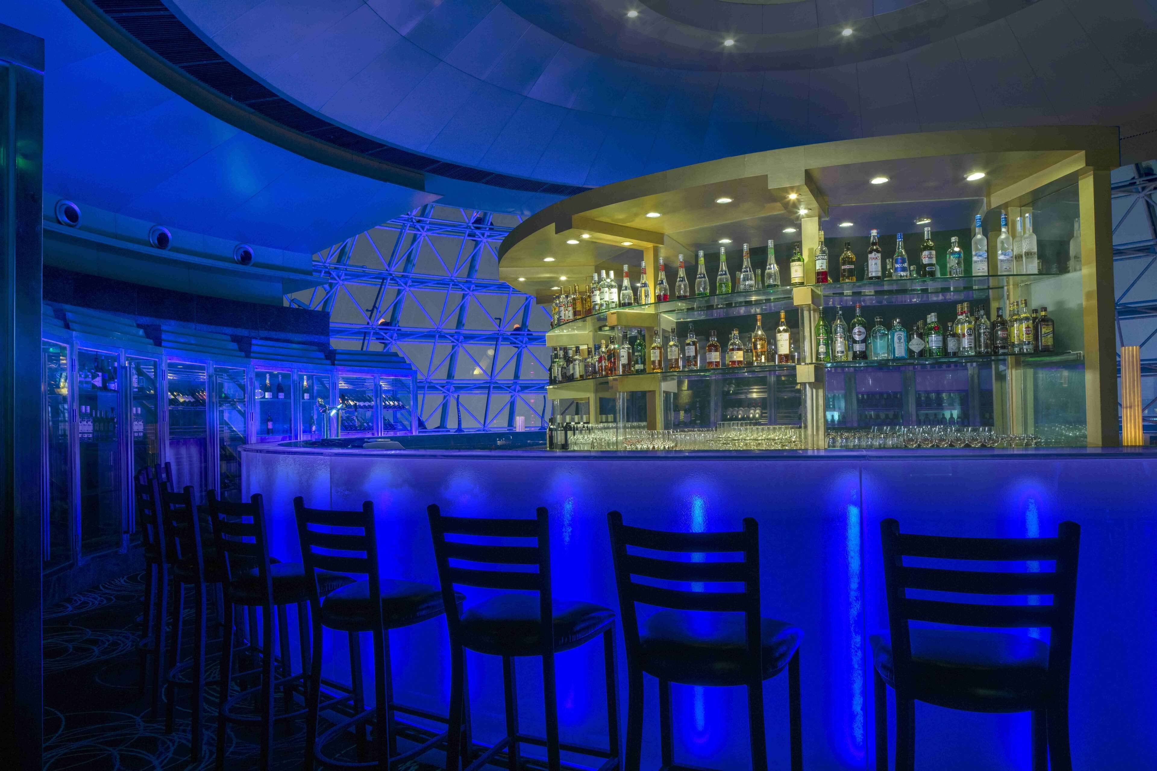 A bar area with a curved counter, multiple shelves of liquor bottles, and several bar stools.