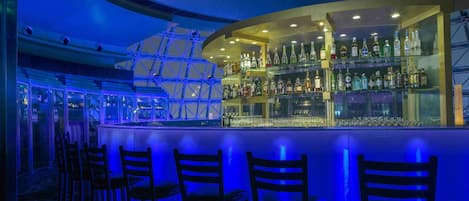 A bar area with a curved counter, multiple shelves of liquor bottles, and several bar stools.