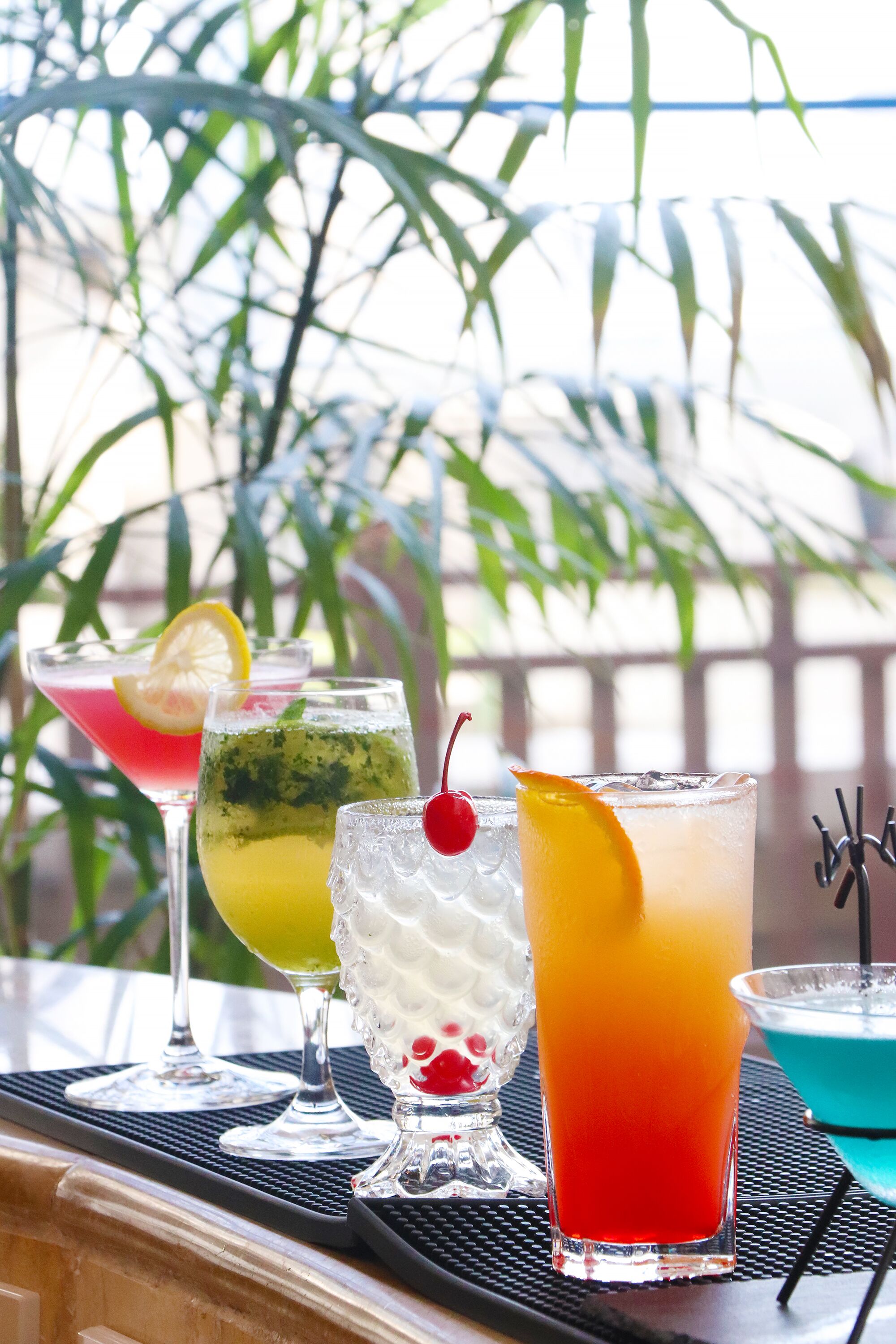 Una mesa con cuatro vasos de diferentes bebidas, un cuenco pequeño de fruta y un adorno.