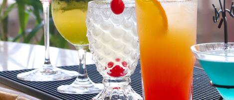 Una mesa con cuatro vasos de diferentes bebidas, un cuenco pequeño de fruta y un adorno.