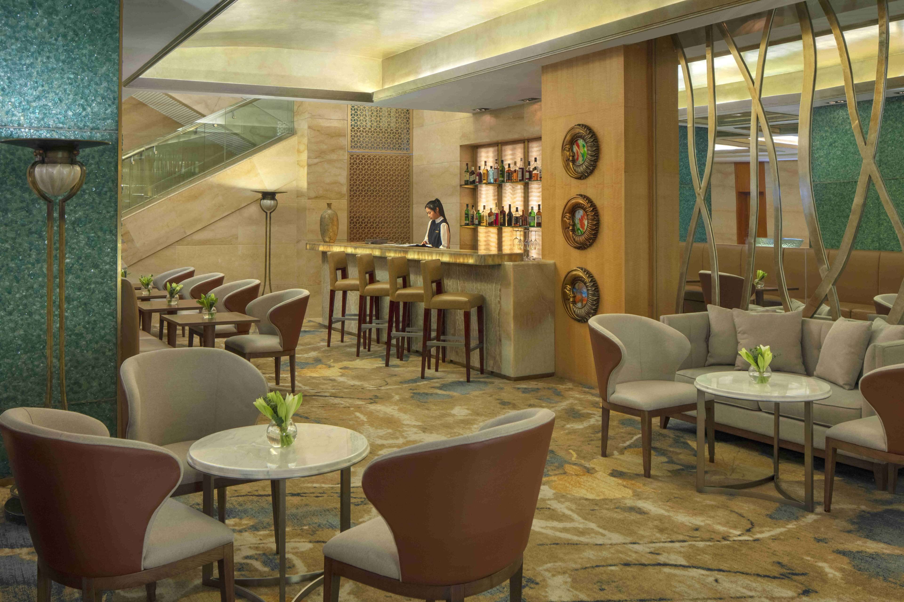 A modern hotel lobby with a bar area, seating arrangements, and a staircase.