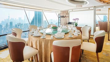 A dining area with a table set for six, large windows offering a city skyline view, and a high ceiling with a circular light fixture.