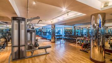 A modern gym with various exercise equipment, wooden flooring, and large mirrors.