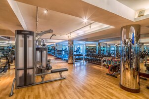 A modern gym with various exercise equipment, wooden flooring, and large mirrors.