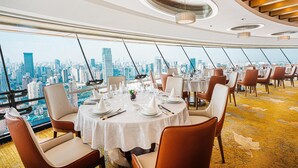 A dining area with round tables set for a meal, large windows offering a city skyline view, and a modern ceiling design. - Radisson Blu Hotel Shanghai New World (Shanghai)