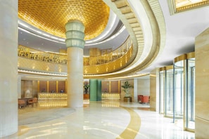 Un hall d’entrée spacieux avec une colonne centrale, un comptoir d’accueil et un ascenseur en verre.