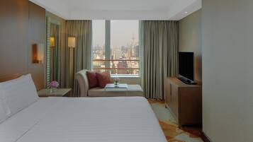 A hotel room with a large bed, a sofa, a TV, and a view of the cityscape.