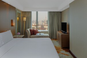 A hotel room with a large bed, a sofa, a TV, and a view of the cityscape.