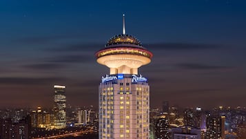 Un edificio alto con señalización iluminada y una estructura superior distintiva, rodeado de un paisaje urbano nocturno.