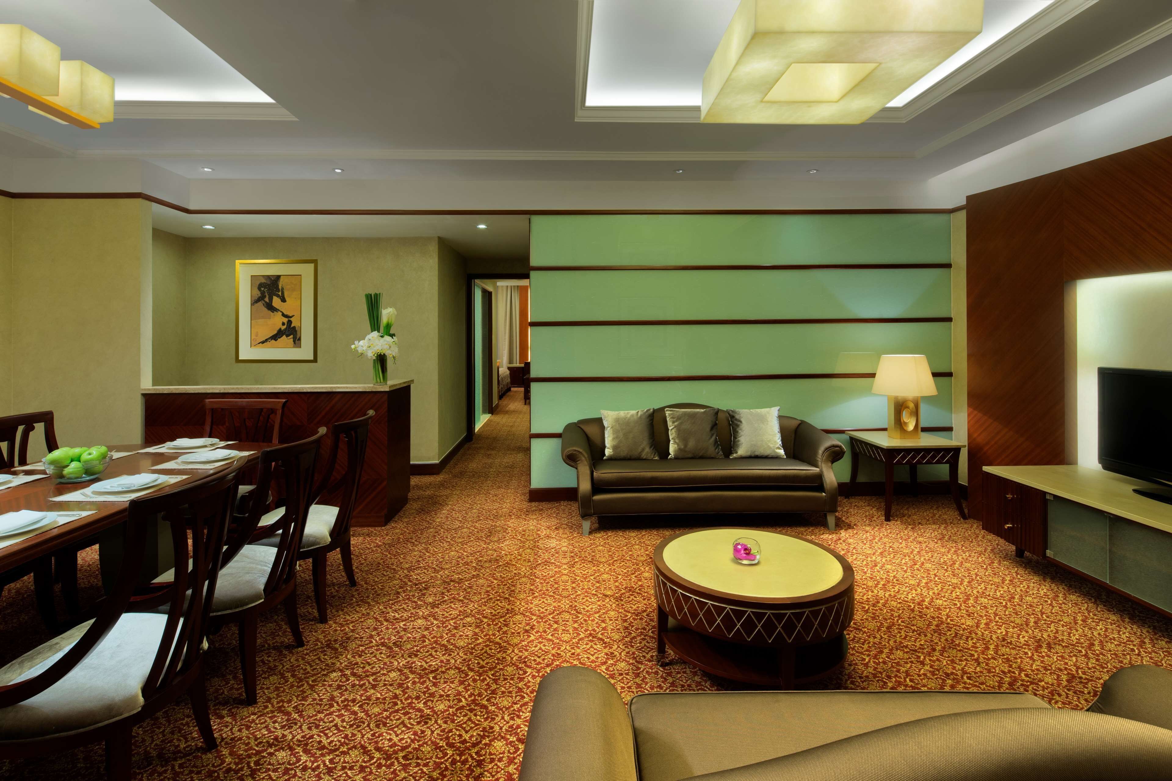 Une chambre d’hôtel comprenant un coin repas, un salon avec un canapé et une télévision, et un sol recouvert de moquette.