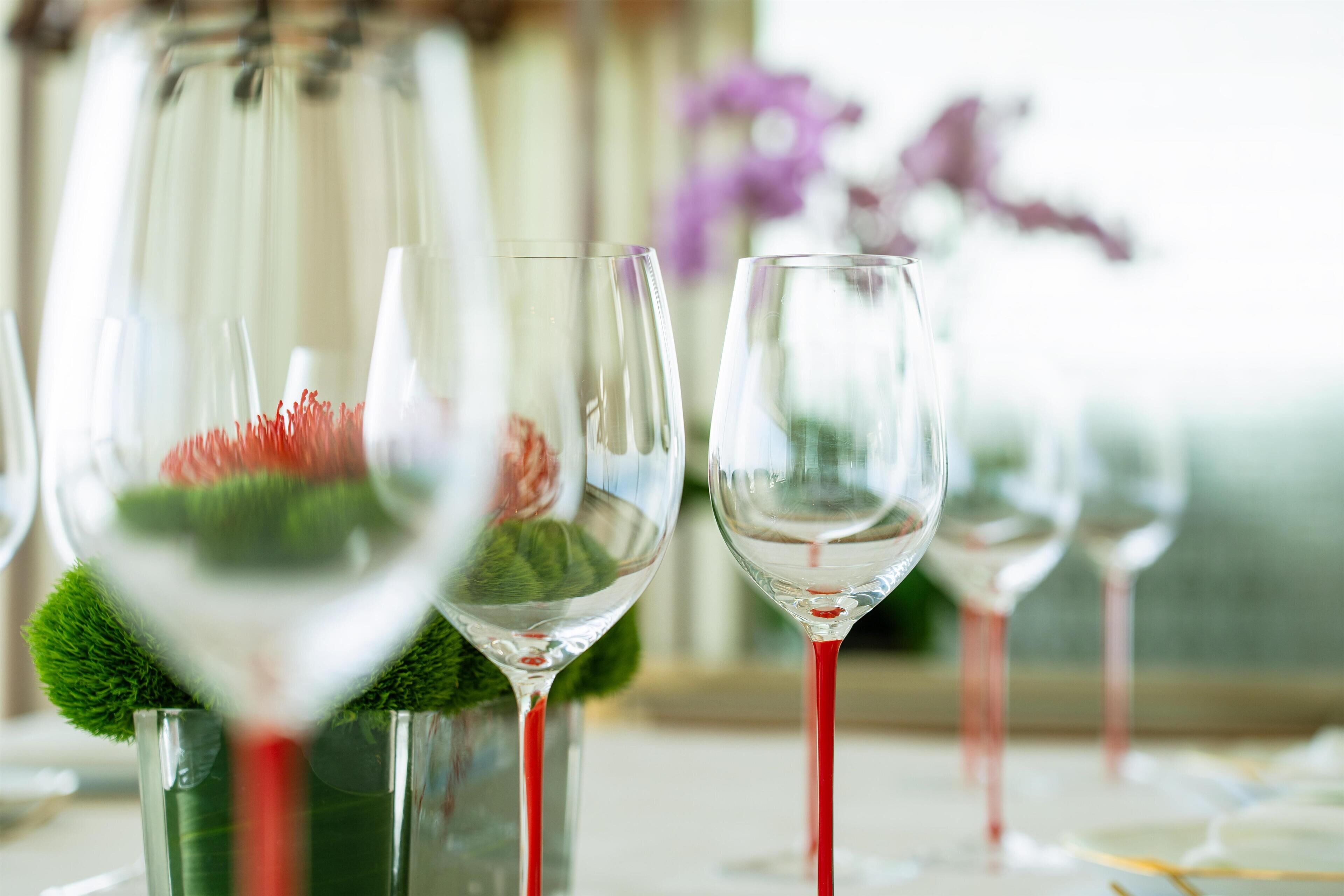 A row of wine glasses with a green brush and a purple flower in the background.
