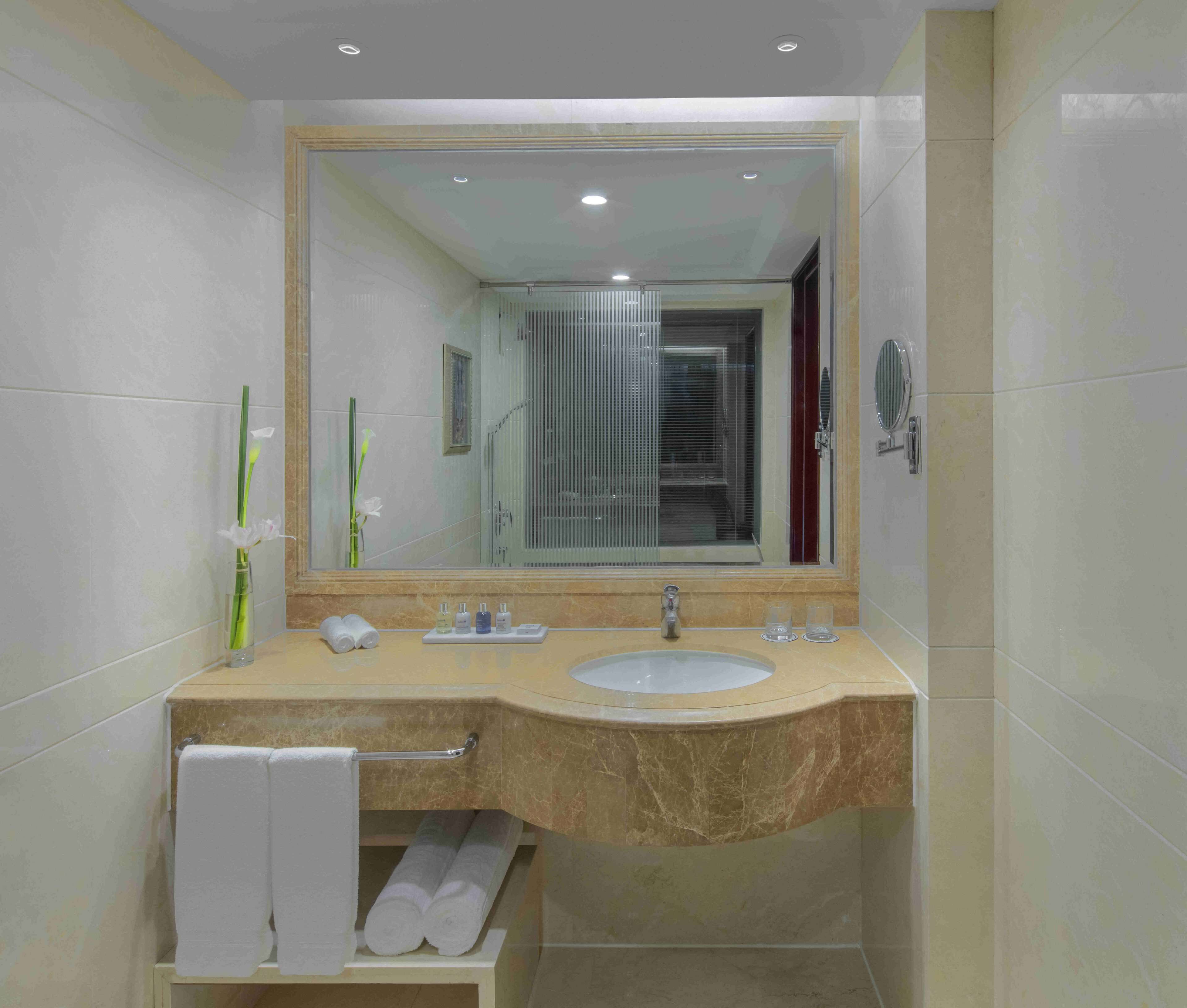 A modern bathroom with a marble sink, a large mirror, and a glass shower enclosure.