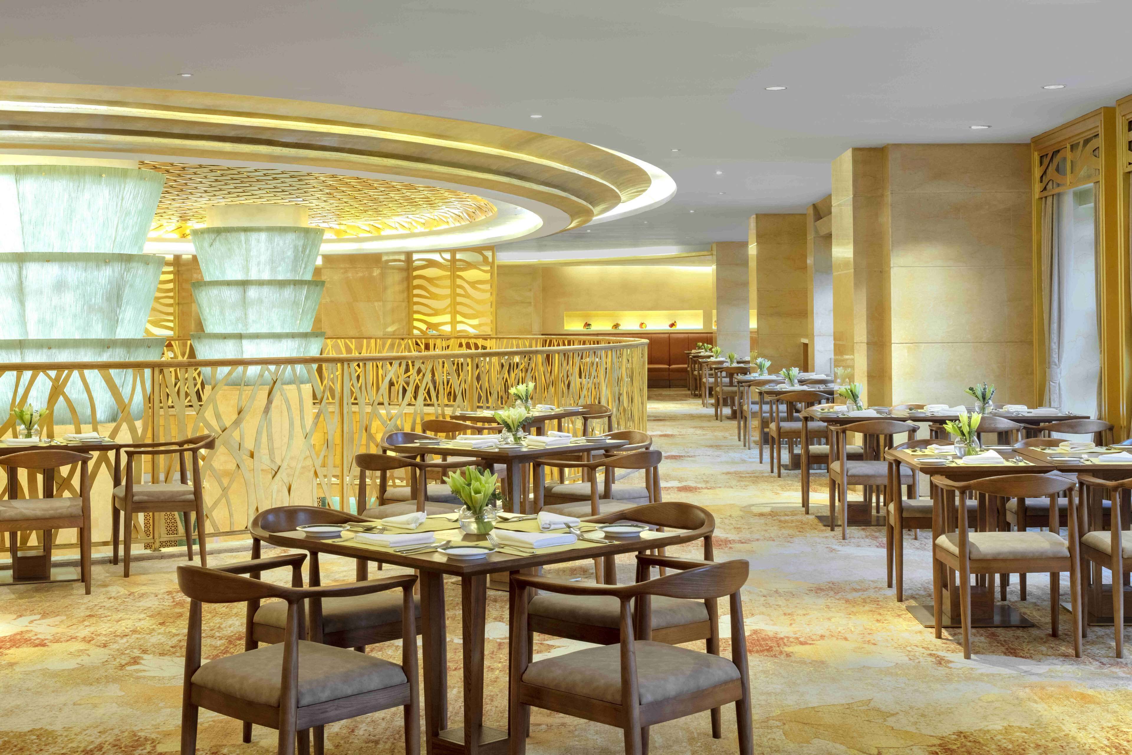 Een ruime hotellobby met meerdere eettafels en stoelen, een decoratieve houten scheiding en een grote kolom.