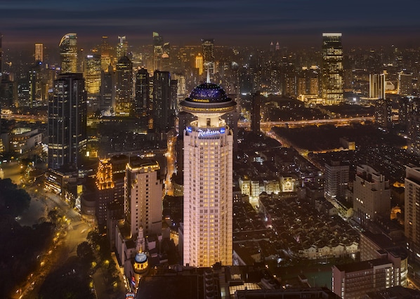 A high-rise hotel with a distinctive dome and illuminated signage, surrounded by a dense urban skyline at night. - Radisson Blu Hotel Shanghai New World (Shanghai)