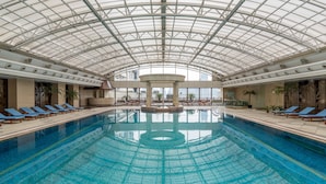 An indoor swimming pool with a glass ceiling, lounge chairs, and palm trees. - Radisson Blu Hotel Shanghai New World (Shanghai)