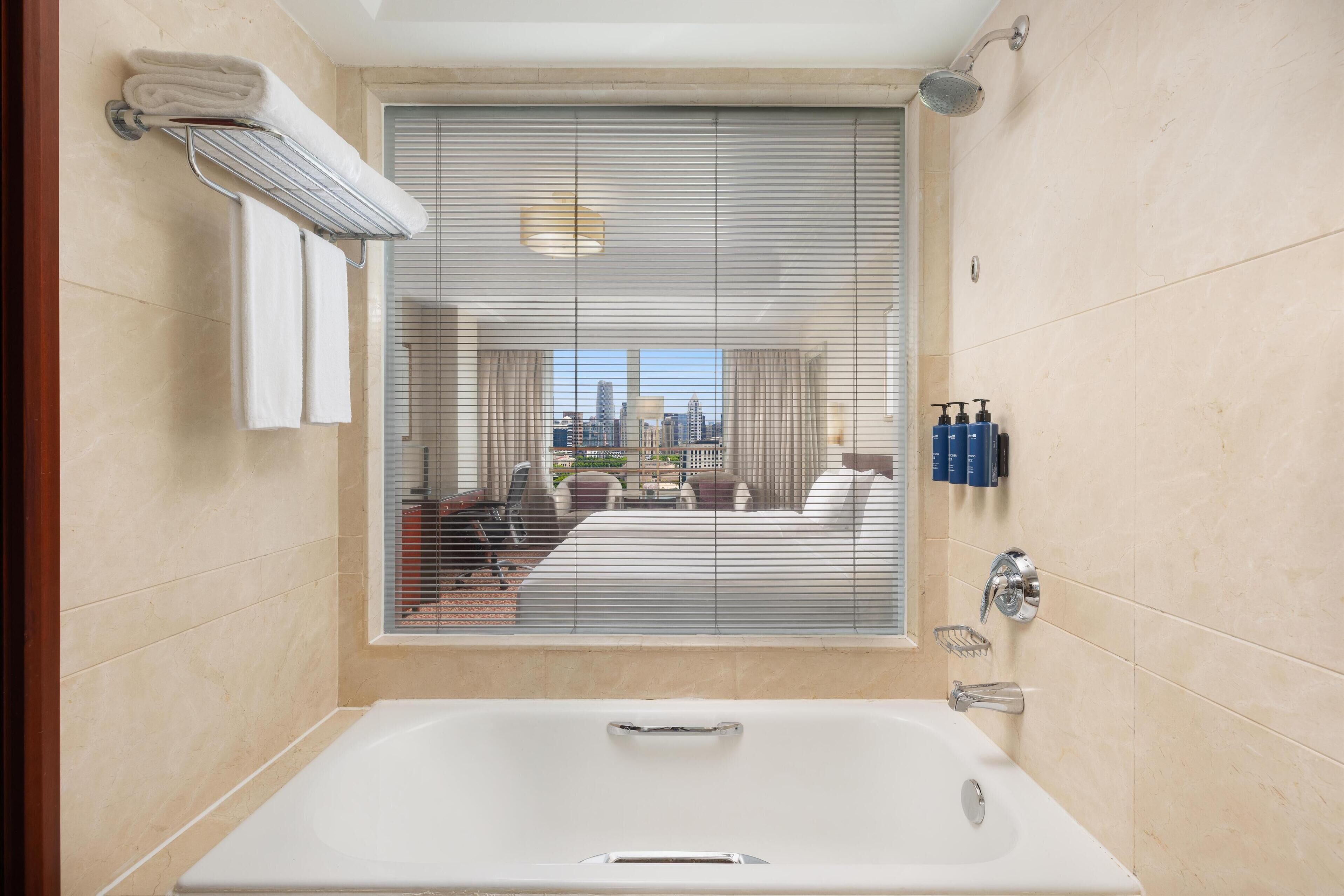 A modern bathroom with a large bathtub, a towel rack, and a window with blinds.