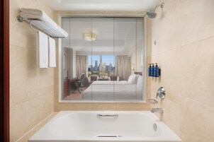 A modern bathroom with a large bathtub, a towel rack, and a window with blinds.