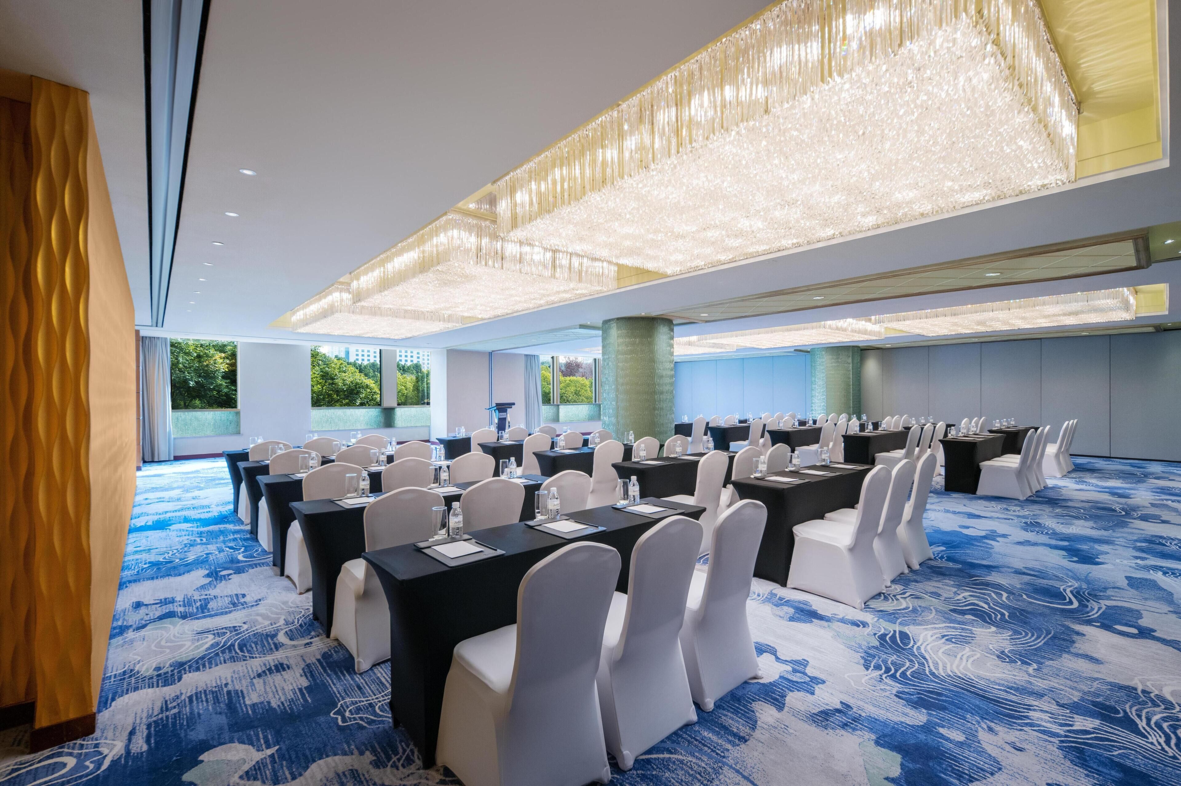 A conference room with tables and chairs, large windows, and a blue patterned carpet.