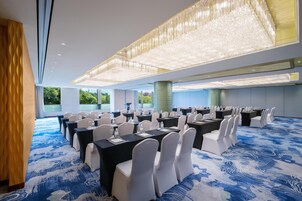 A conference room with tables and chairs, large windows, and a blue patterned carpet.