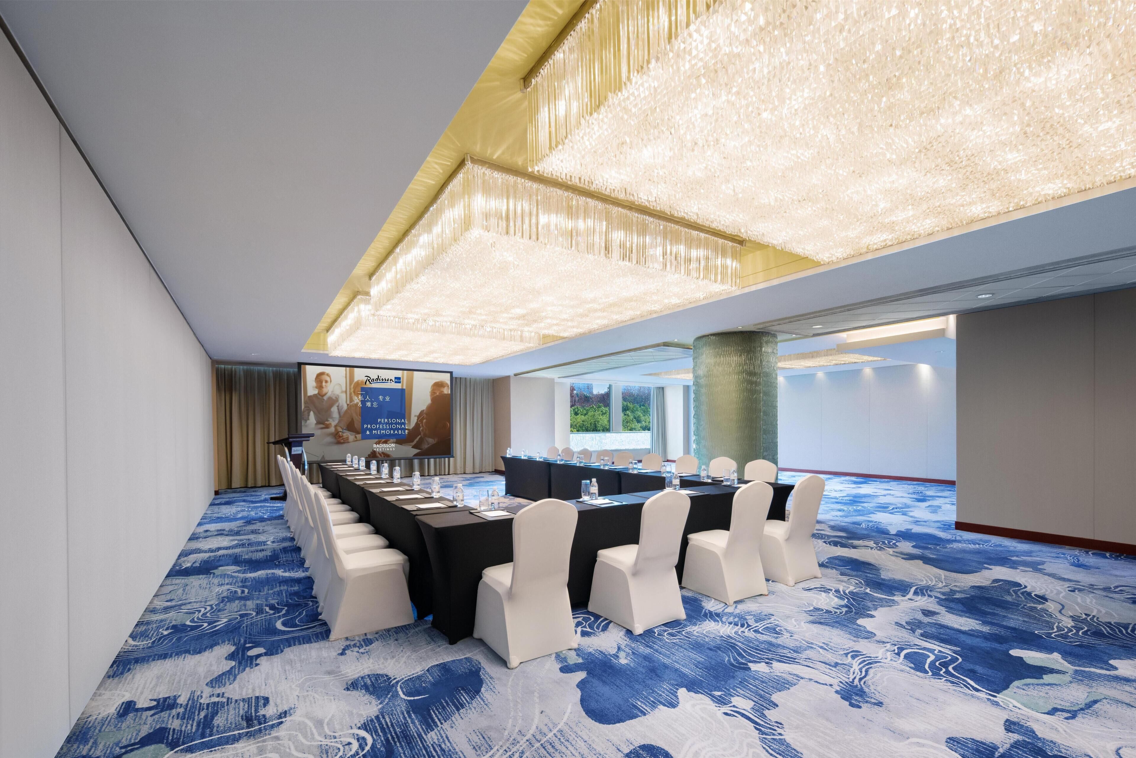 A conference room with a long table, white chairs, and a blue patterned carpet.