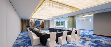 A conference room with a long table, white chairs, and a blue patterned carpet.
