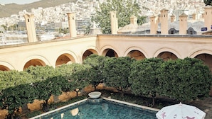 Schwimmbeckenbereich mit klarem Wasser, umgeben von Grünpflanzen und Blick auf eine Stadtlandschaft mit Gebäuden und einer Moschee.