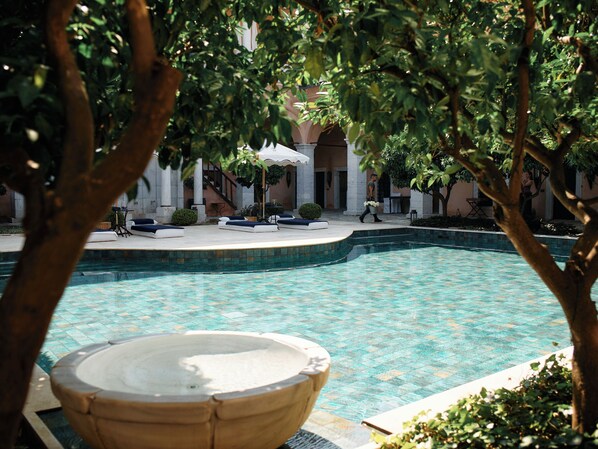 A swimming pool with lounge chairs and a hot tub, surrounded by trees and a building with columns.