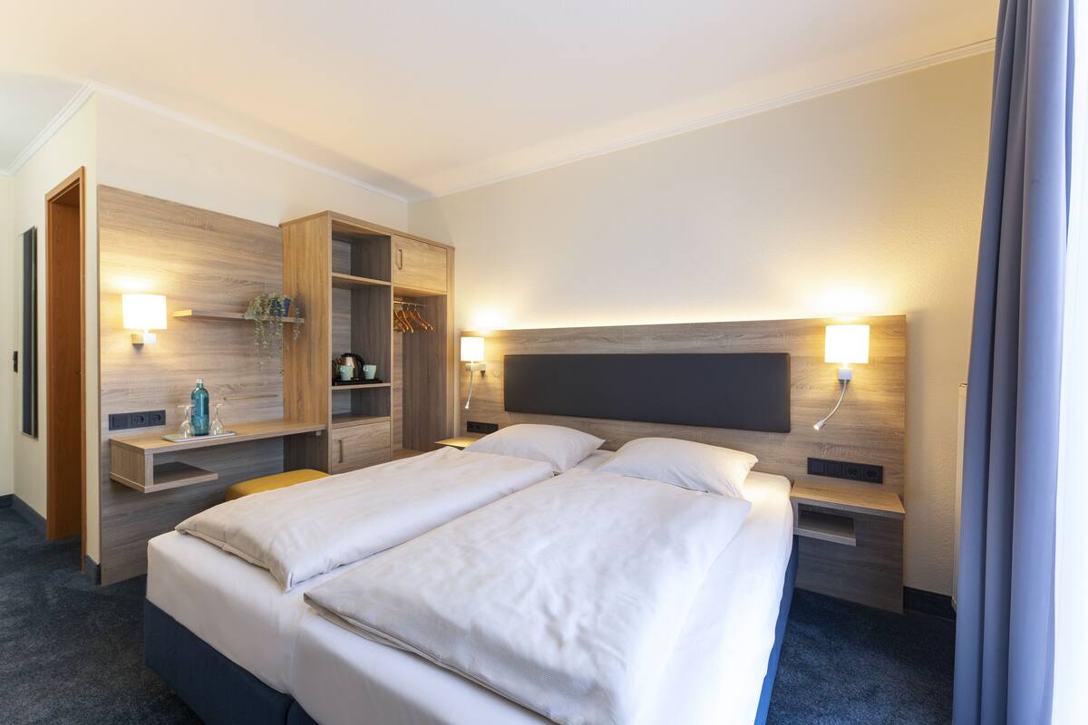 A hotel room with a large bed, a wooden wardrobe, bedside tables, and wall-mounted lamps.
