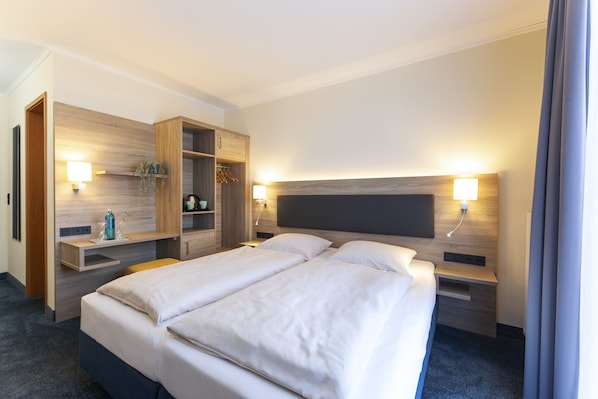 A hotel room with a large bed, a wooden wardrobe, bedside tables, and wall-mounted lamps.