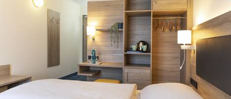 Habitación de hotel con dos camas, un armario de madera, un escritorio pequeño y una estantería con lámpara.