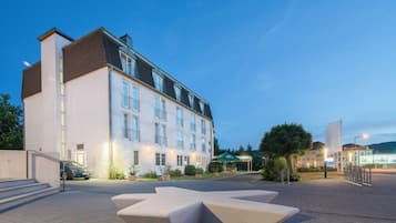 Ein Hotel mit modernem Design, das eine markante Eingangshalle mit Treppen und einen großzügigen Sitzbereich im Vordergrund zeigt.