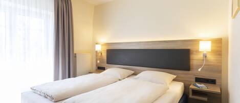 A double bed with white linens, a bedside table with a lamp, and a wall-mounted light fixture.
