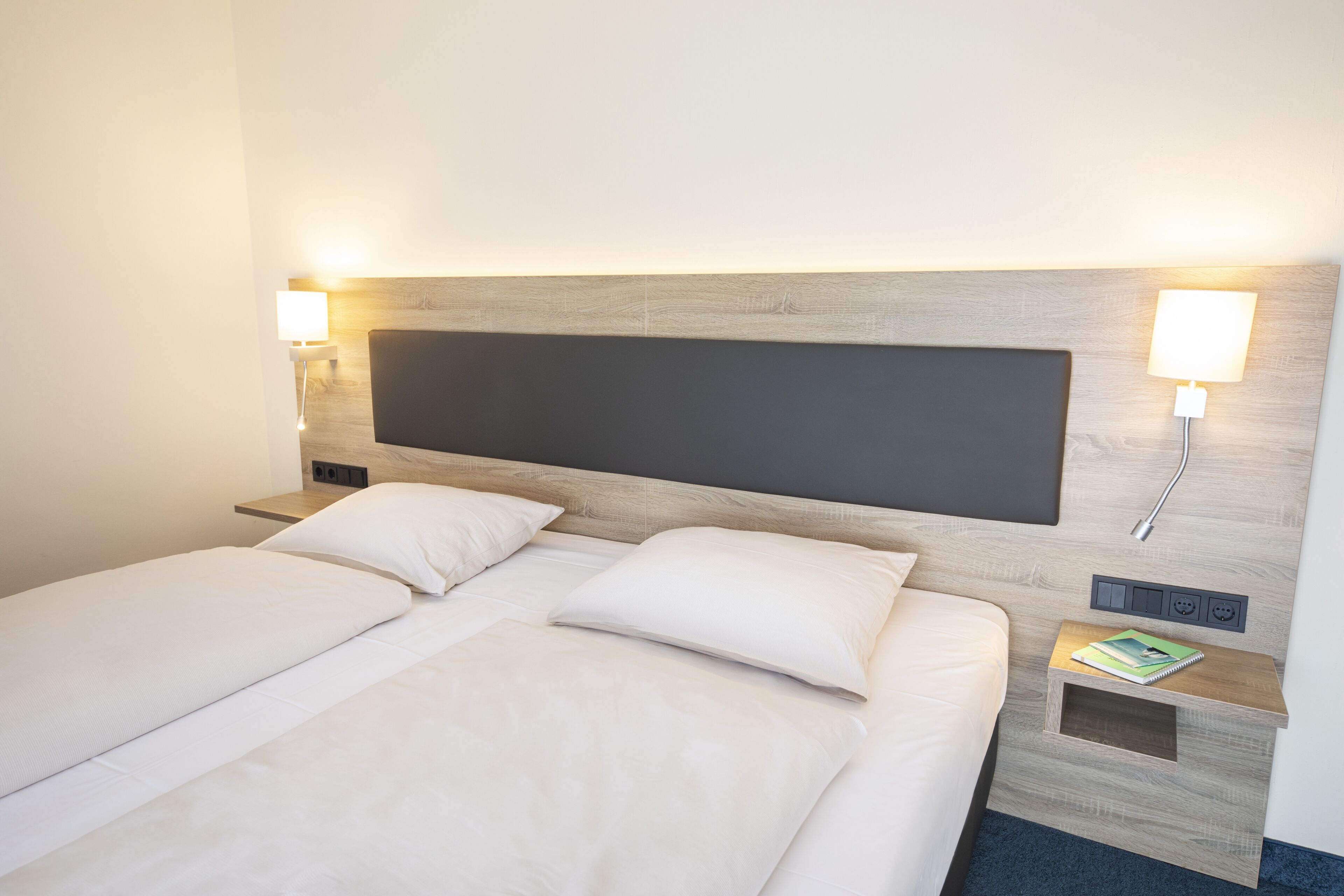A hotel room with a large bed, two bedside tables, a nightstand, and a wall-mounted lamp.