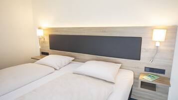 A hotel room with a large bed, two bedside tables, a nightstand, and a wall-mounted lamp.