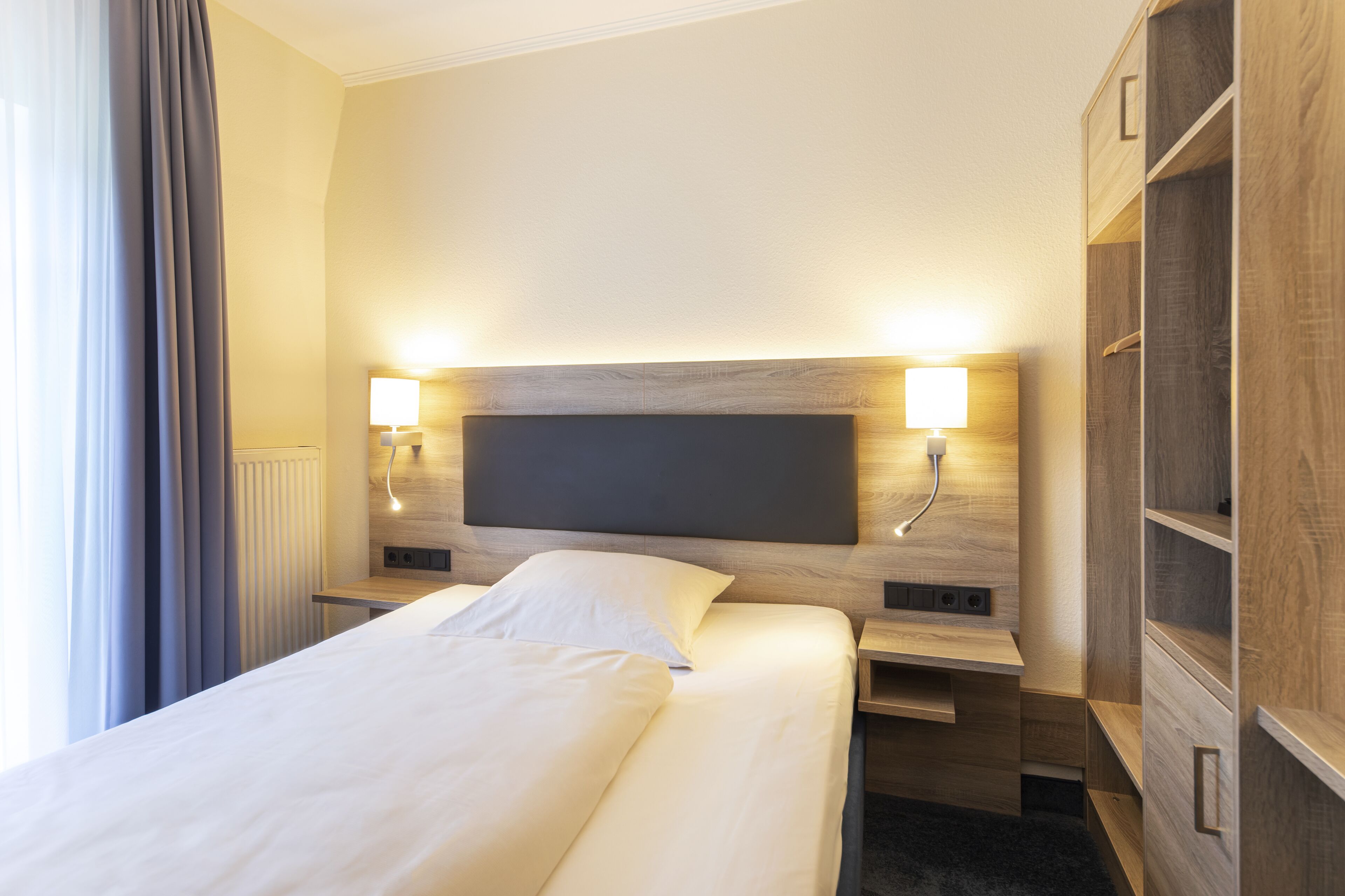 Ein Hotelzimmer mit einem großen Bett, Nachttischlampen, einem Holz-Kopfteil und eingebauten Regalen.