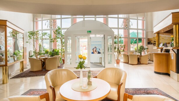 Un hall d’entrée spacieux avec une table ronde centrale, des sièges confortables et des plantes en pot.