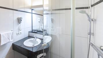Ein modernes Badezimmer mit zwei Waschbecken, einer Duschkabine aus Glas und einem an der Wand befestigten Föhn.