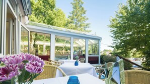 Une terrasse extérieure avec des meubles en osier, une véranda et un vase bleu posé sur une table.