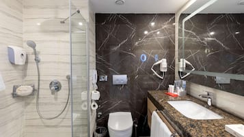 A modern bathroom with a glass-enclosed shower, a marble-tiled wall, a sink with a granite countertop, and a mirror.