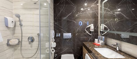 Un baño moderno con ducha de vidrio, pared con azulejos de mármol, lavamanos con encimera de granito y espejo.