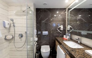 Un baño moderno con ducha de vidrio, pared con azulejos de mármol, lavamanos con encimera de granito y espejo.