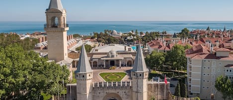 A historic castle with two prominent towers, a central courtyard, and a view of the sea.