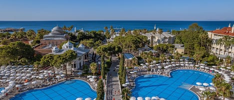 A resort with two large swimming pools, palm trees, and a view of the sea.