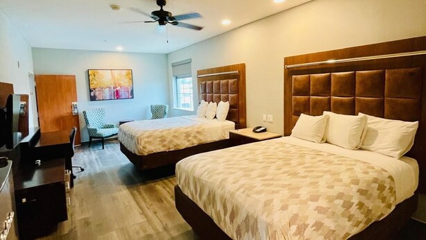 A hotel room with two beds, a desk, a chair, a ceiling fan, and a painting on the wall. - Americas Best Value Inn La Porte (La Porte)