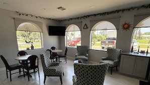 A spacious room with a dining area, several patterned chairs, a TV mounted on the wall, and large windows with a view of the outside. - Americas Best Value Inn La Porte (La Porte)