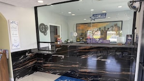 A reception area with a marble counter, a welcome sign, and a cityscape view through the window. - Americas Best Value Inn La Porte (La Porte)