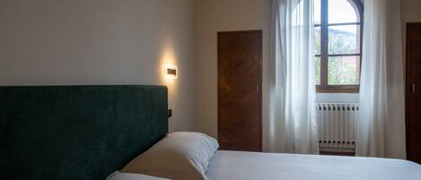 A bedroom with a bed, a headboard, a window with curtains, and a wall-mounted light.