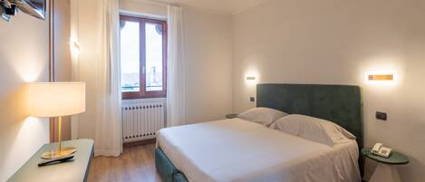 Une chambre d’hôtel avec un lit, une table de chevet, une lampe et une vue sur la ville par la fenêtre.