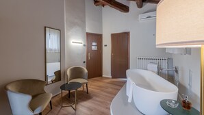 Un baño moderno con una bañera independiente, un espejo redondo y una mesita con una botella.